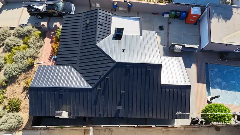 Top-down view of black standing seam roof planes beside a low-slope roof section