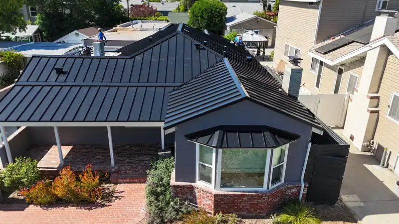 Black standing seam metal roof with a hip roof over a bay window and a wraparound eave
