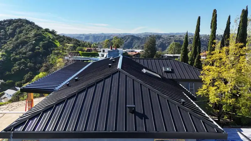 Black standing seam metal roof on a large hillside home, with canyon and mountain views behind