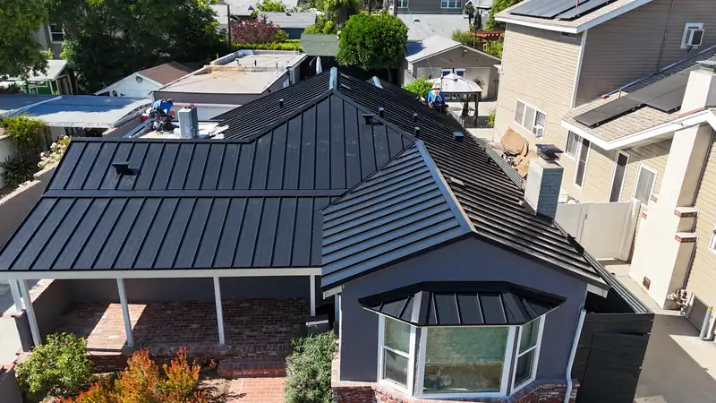 Black standing seam metal roof with hips and a separate panel roof over a bay window