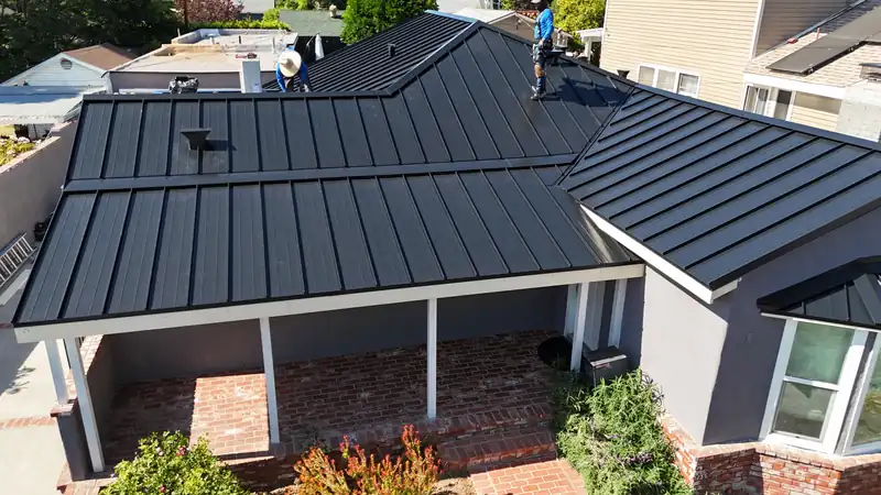 Wide view of a black standing seam roof with a hip, a gable and a covered patio